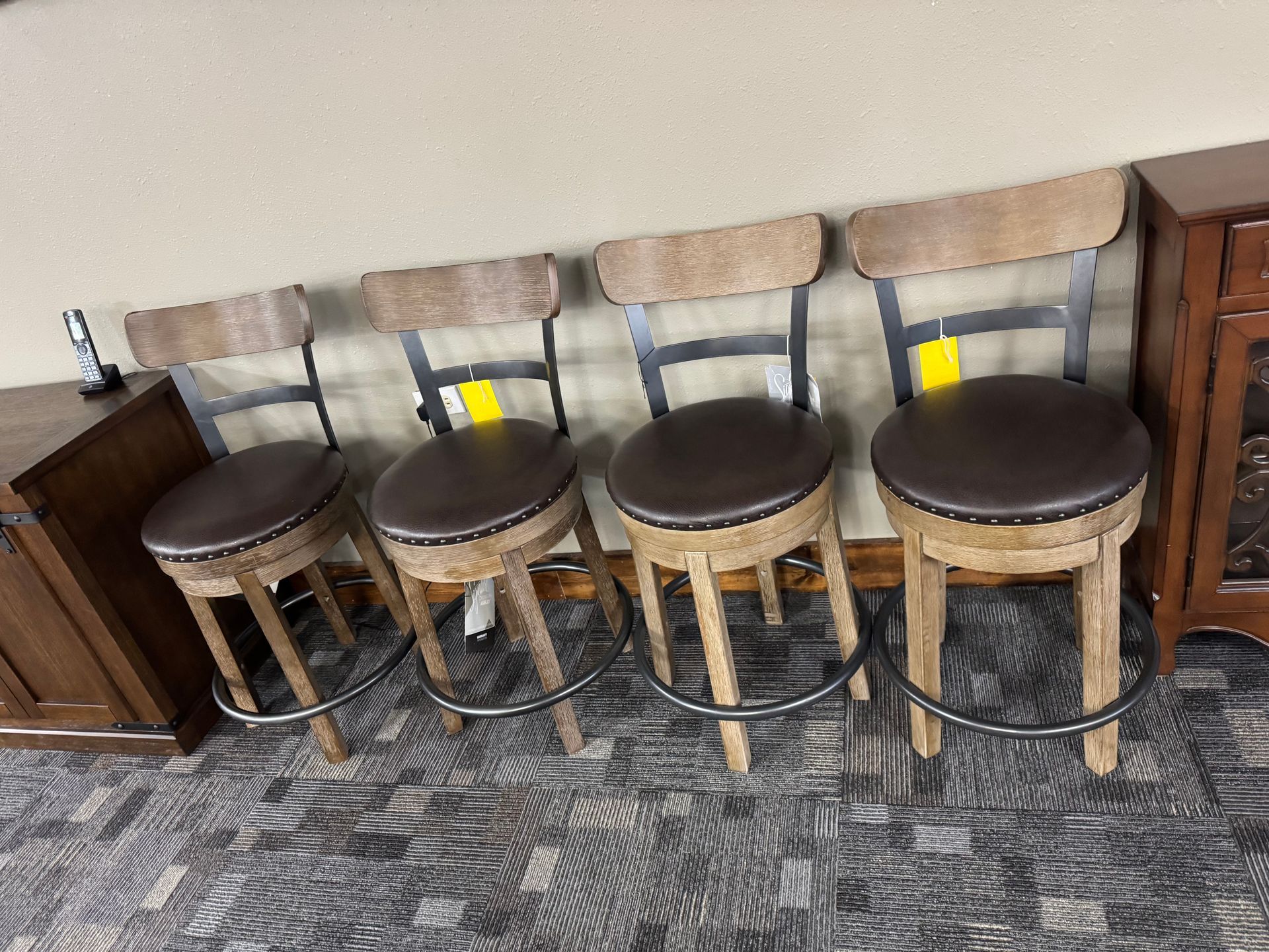 Four brown and tan bar stools with padded seats and backs, set against a wall.