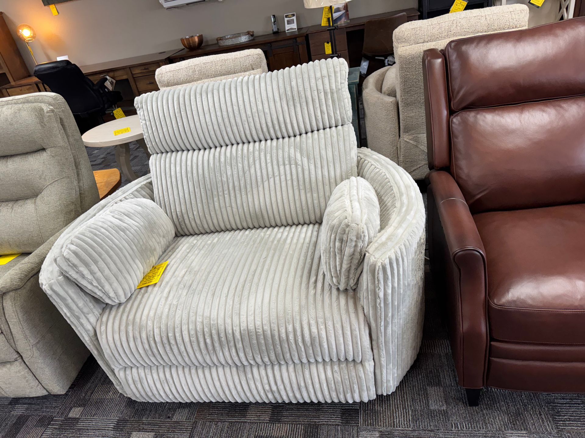 Cream corduroy recliner in a furniture store next to a brown leather recliner.