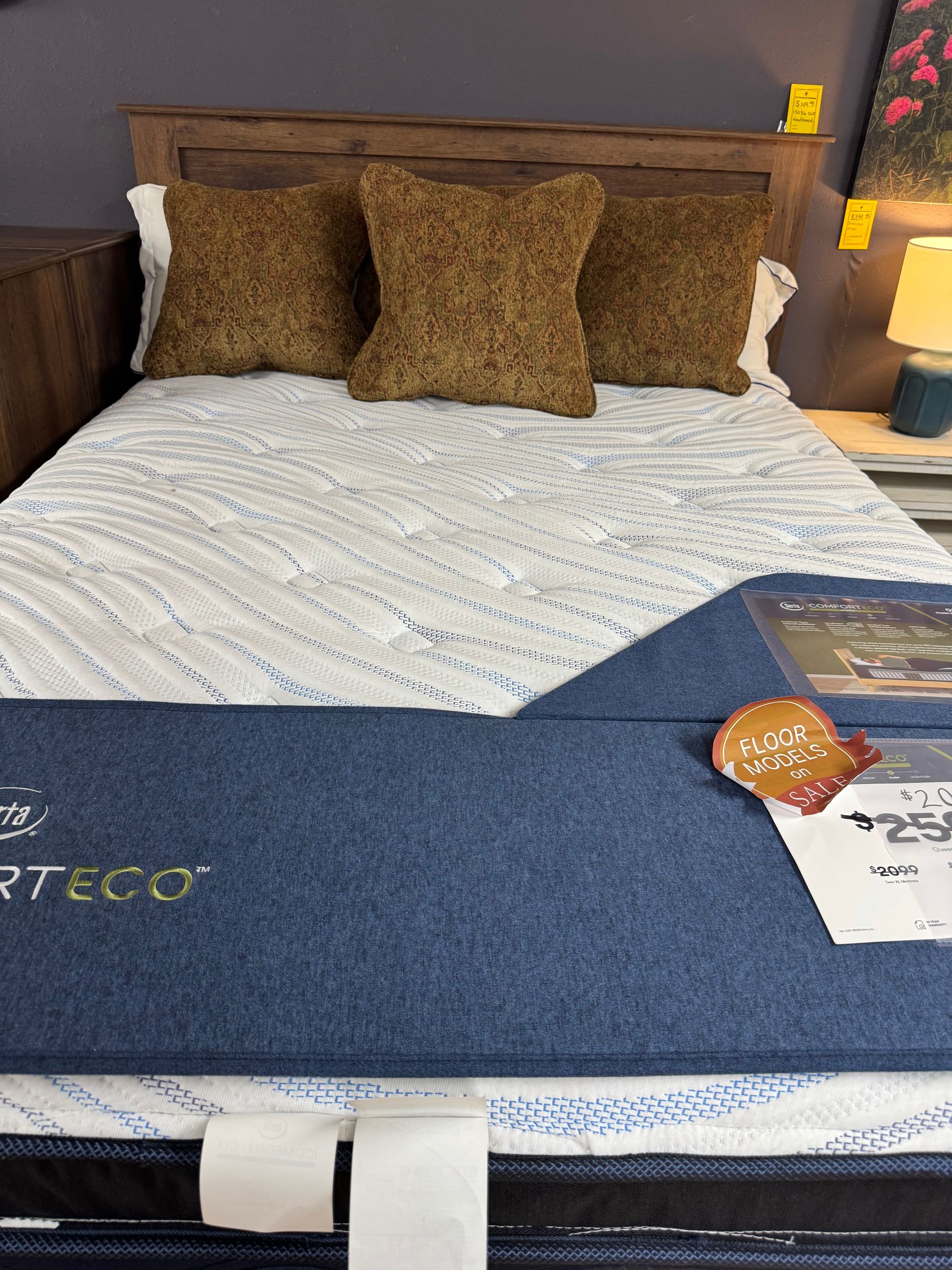 Bed with wooden headboard, white and blue mattress, three brown pillows.