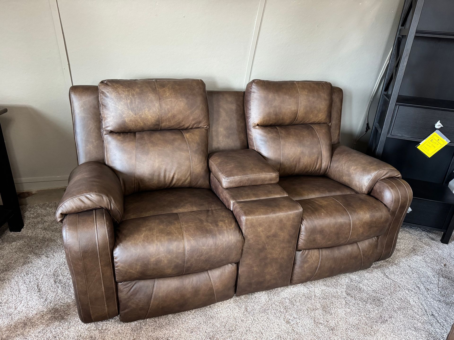 Brown leather reclining loveseat with center console on beige carpet.