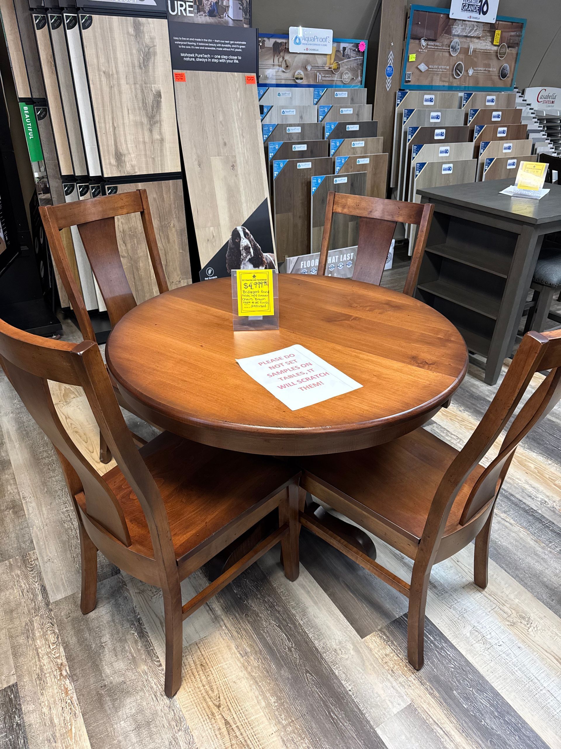 Round wooden dining table with four matching chairs. Retail setting, brown wood.