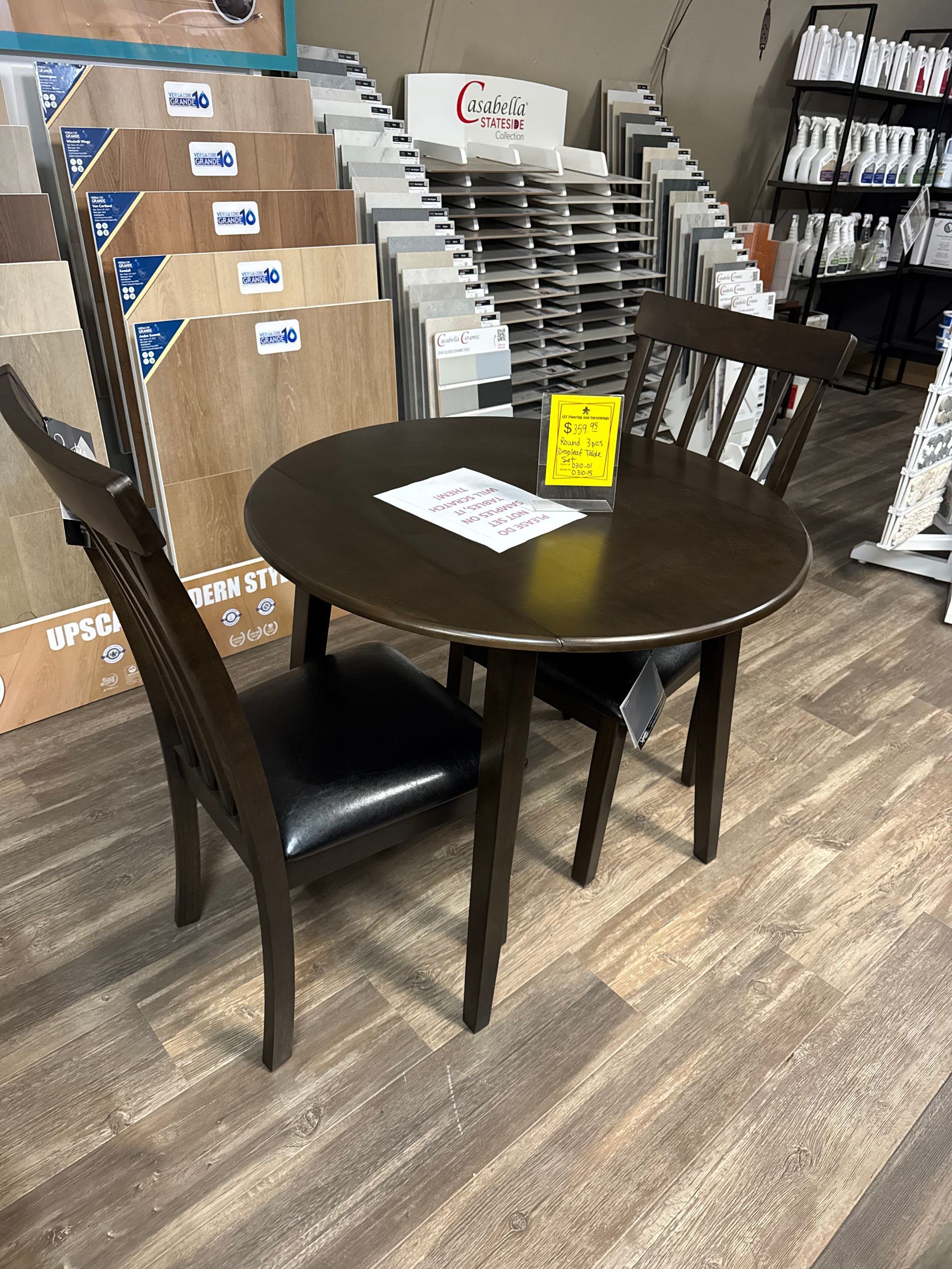 Round dining table with two chairs, displayed in a store with flooring and tile samples.