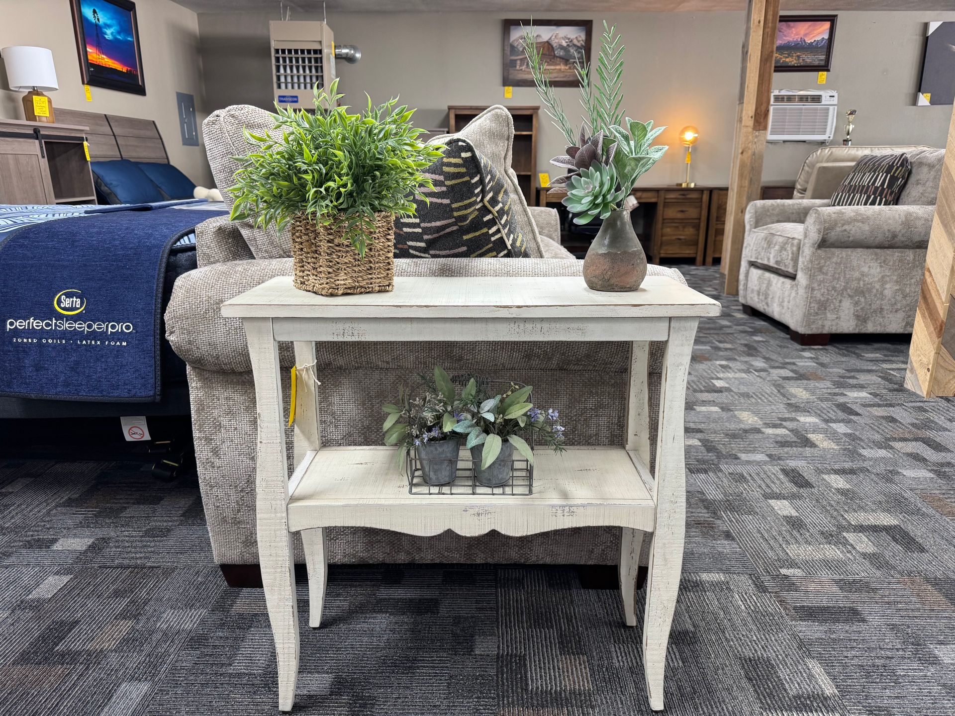 White distressed side table with plants displayed in a furniture store.