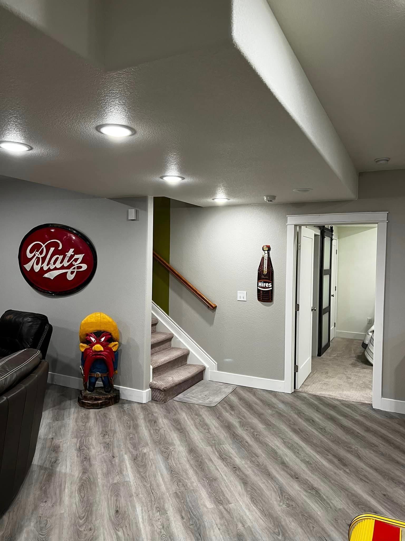 A finished basement with a Blatz sign, stairs, a doorway, and wood-look flooring.