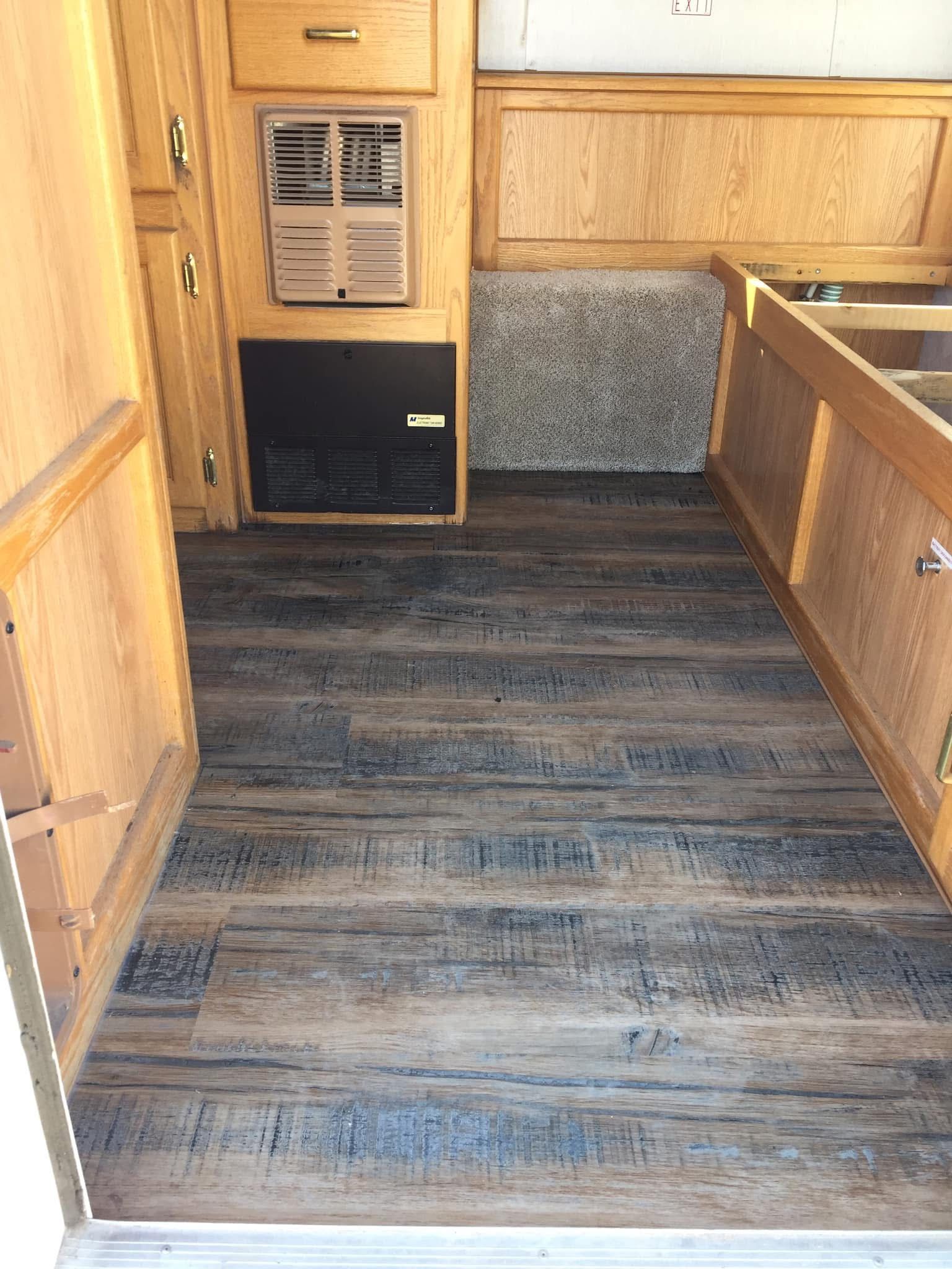Interior of a trailer with wood paneling and wood-look flooring. Contains a heater and cabinet.