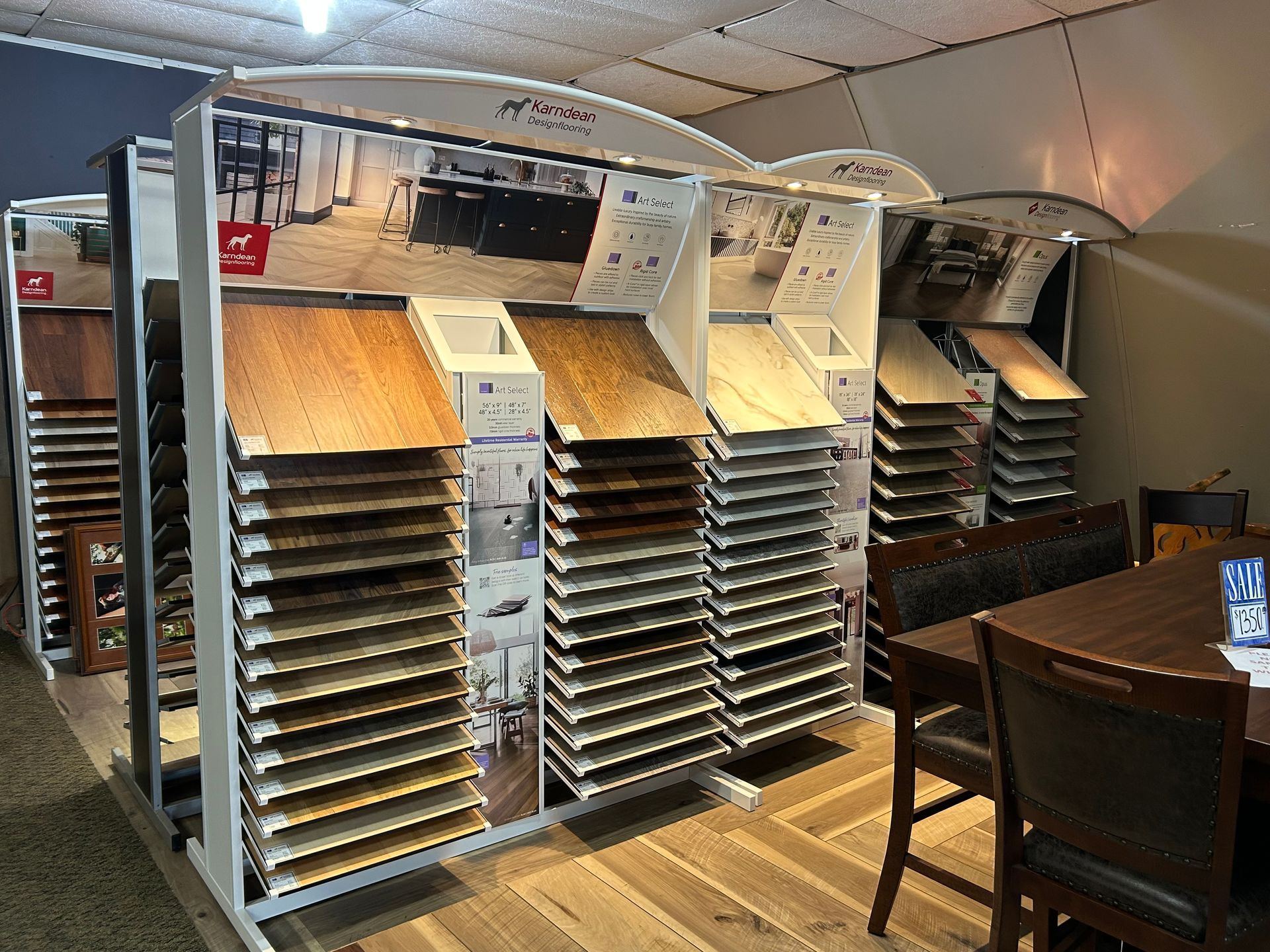 Flooring samples displayed on racks in a showroom, with a table and chairs in the foreground.