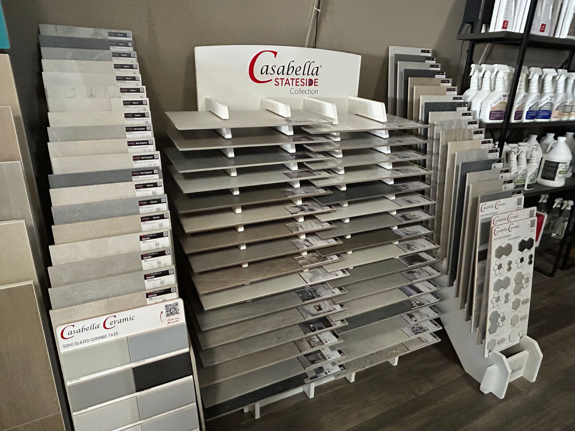 Tile display rack in a store, showcasing various tile samples in shades of gray and beige.