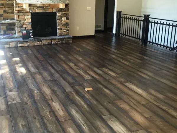 Wood floor in a room with a fireplace and black railing, bathed in sunlight.