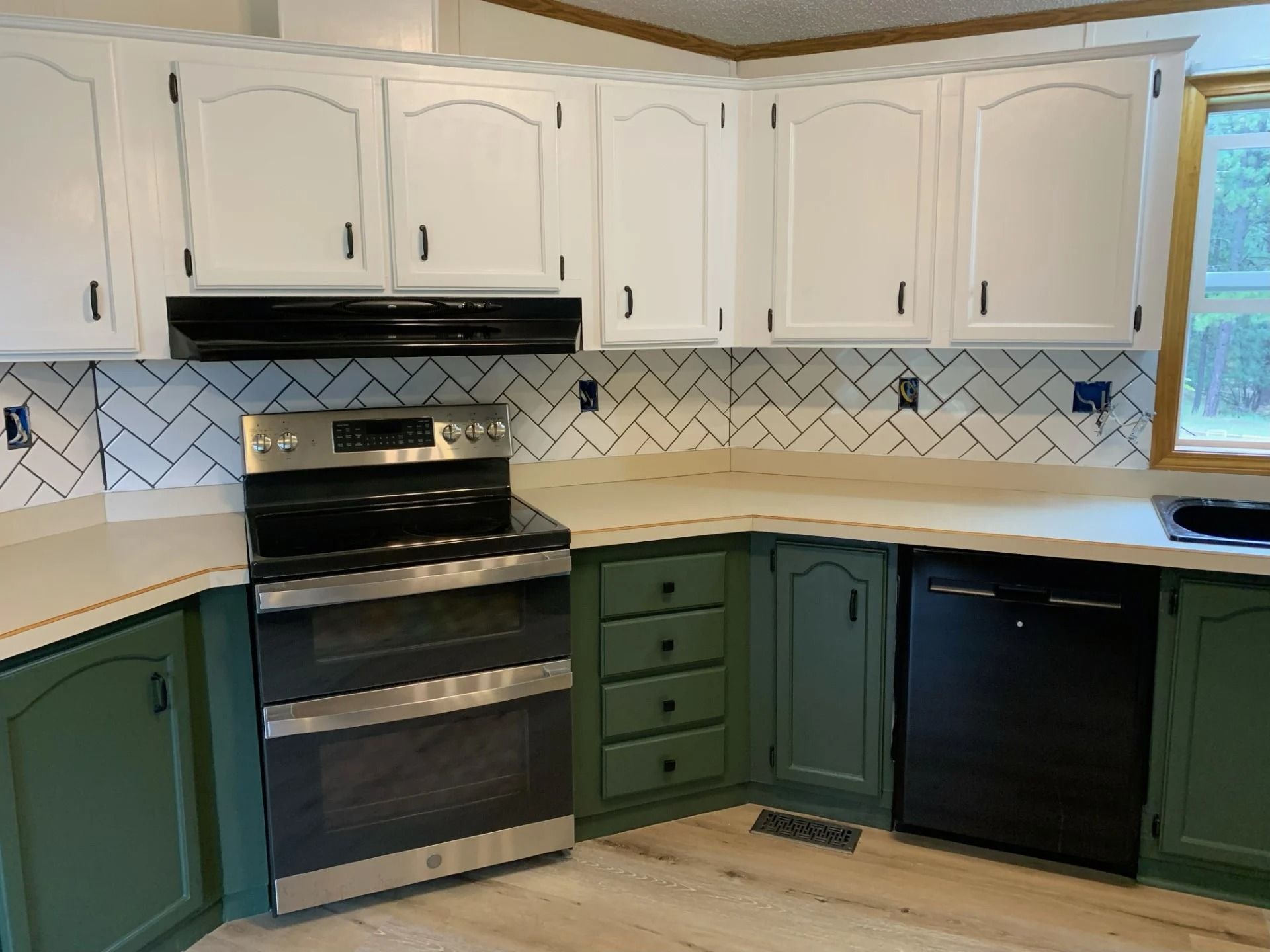 Kitchen with white upper cabinets, green lower cabinets, stainless steel appliances, and a white and gray backsplash.