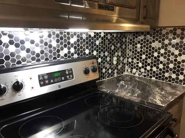 A kitchen with a black stovetop, silver range hood, and honeycomb tile backsplash.