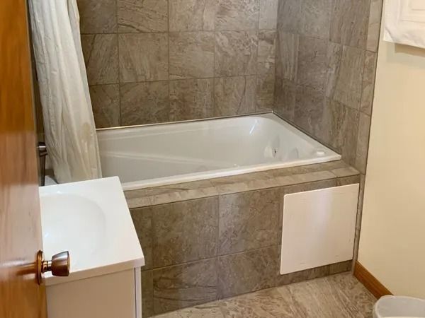 Bathroom with a tiled surround for the bathtub, a vanity and shower curtain.