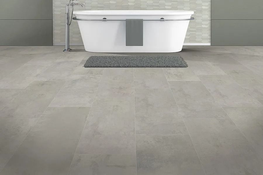 Gray bathroom with a white tub, gray mat, and gray floor tiles.
