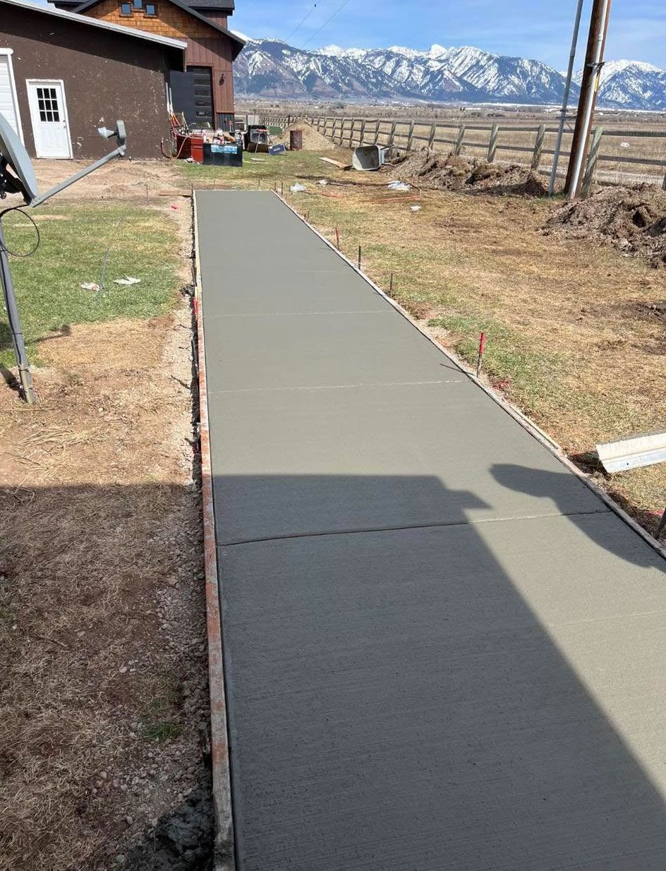 A concrete walkway is being built in front of a house with mountains in the background
