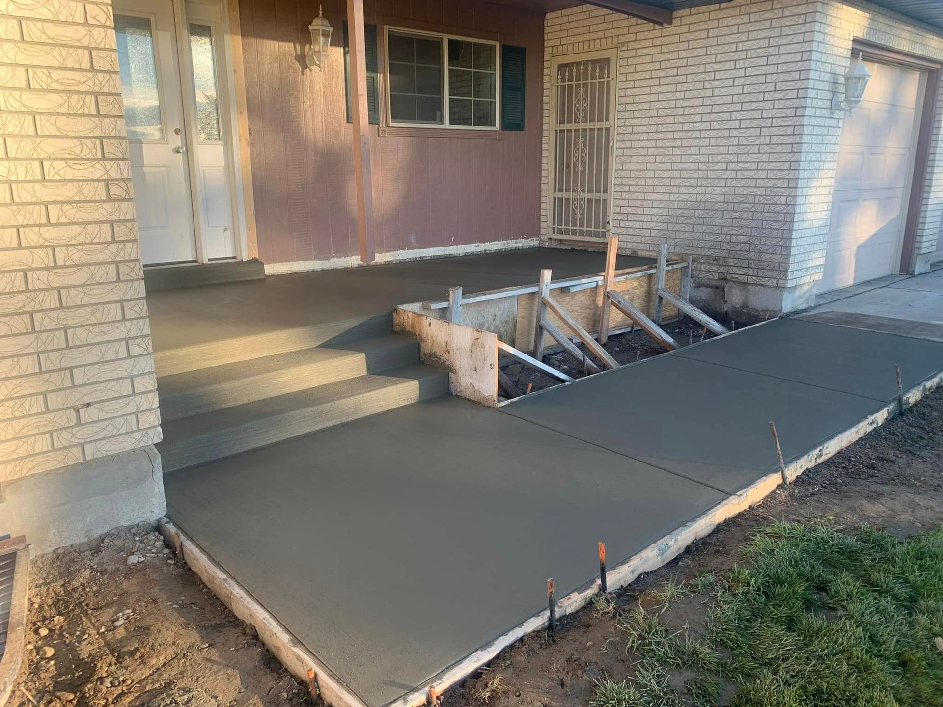 A concrete walkway is being built in front of a brick house