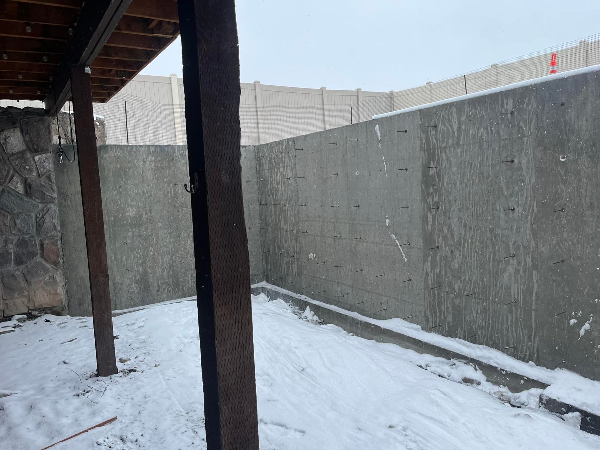 A snowy basement with a concrete wall and wooden posts