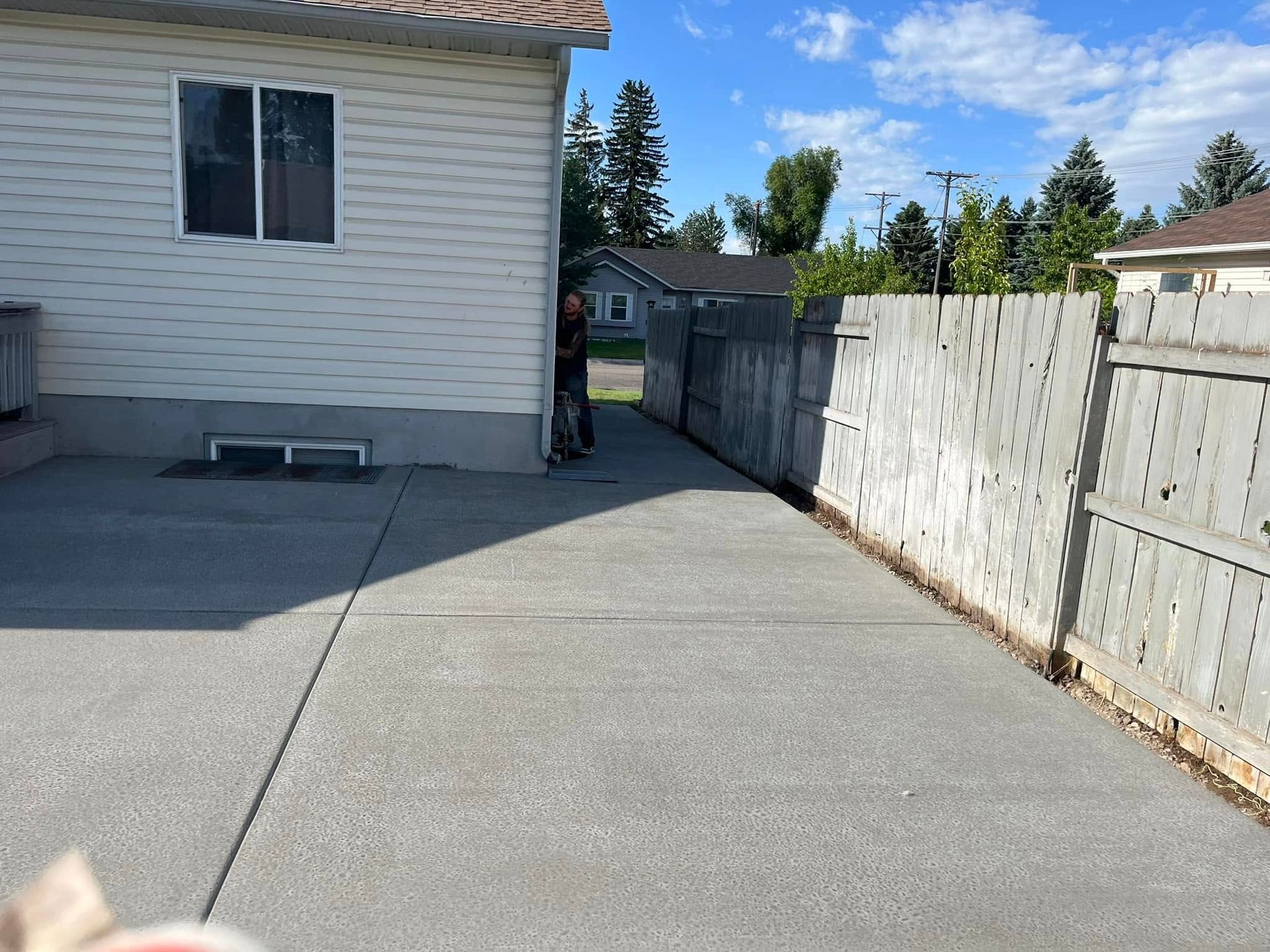 A concrete driveway leading to a house with a wooden fence
