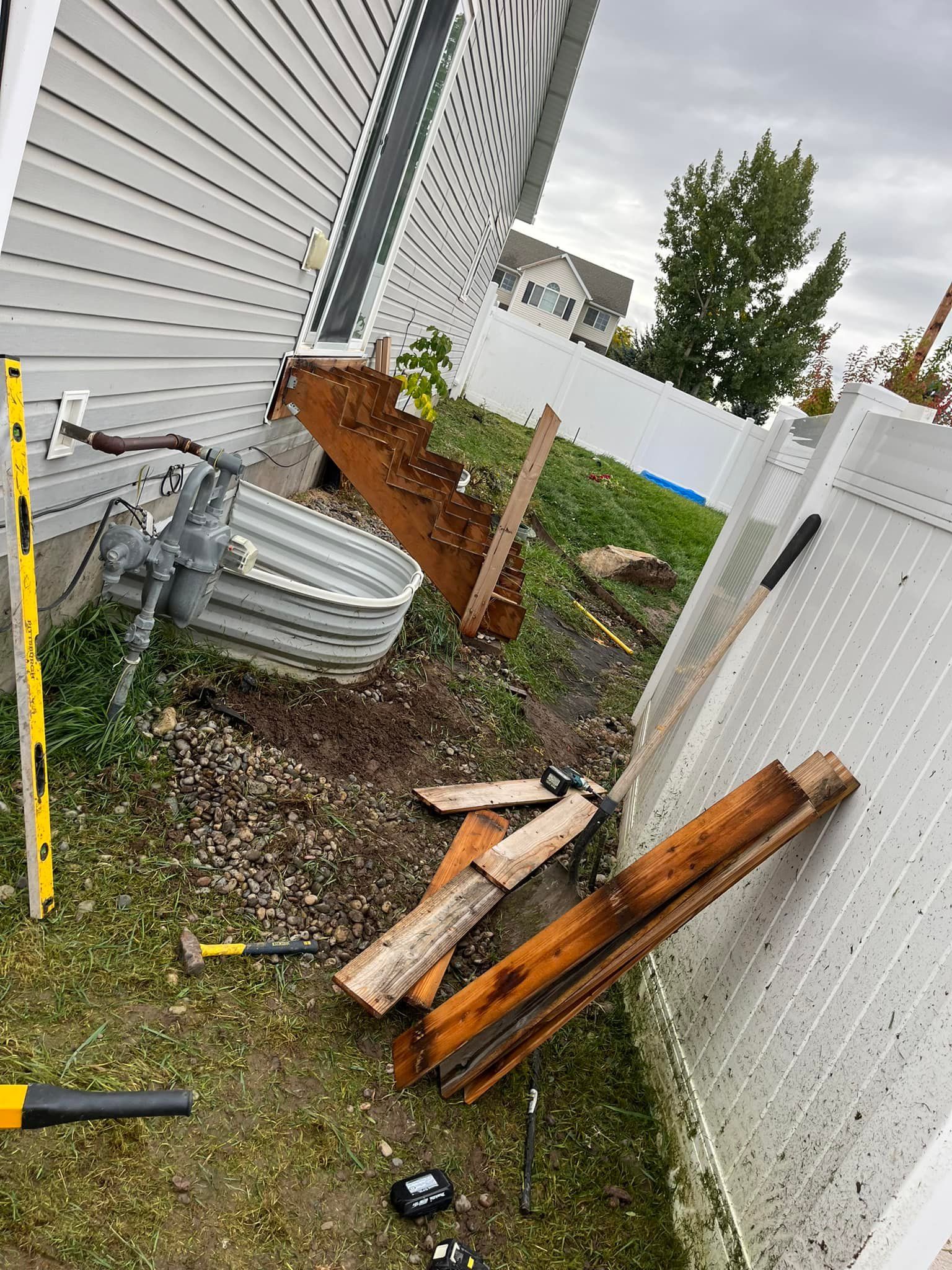 A bunch of wood is laying on the ground next to a white fence