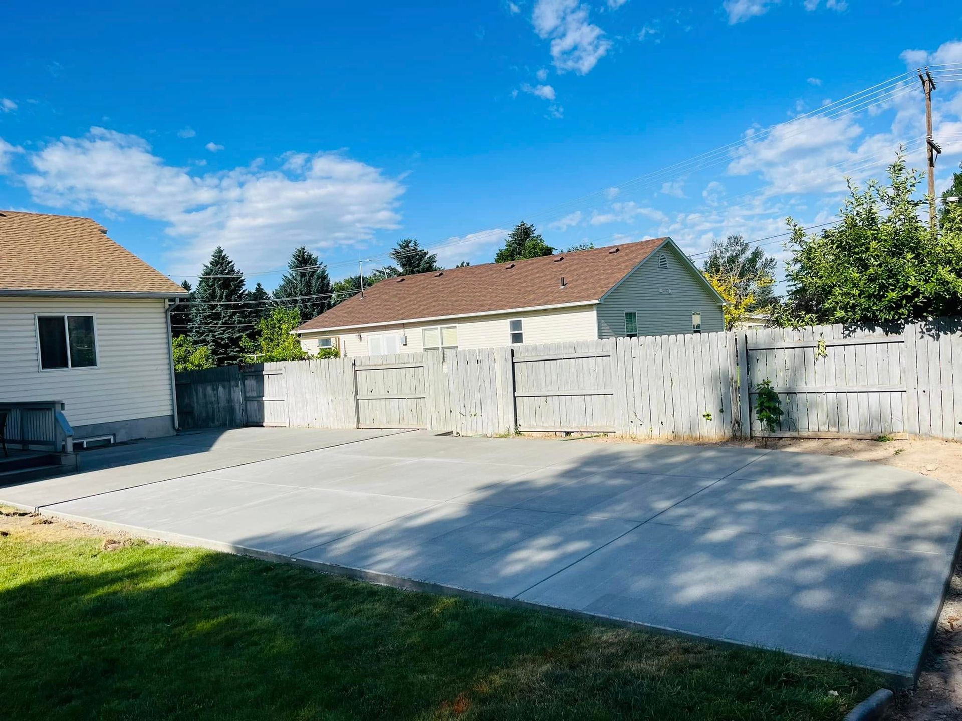 A concrete driveway leading to a house with a white fence