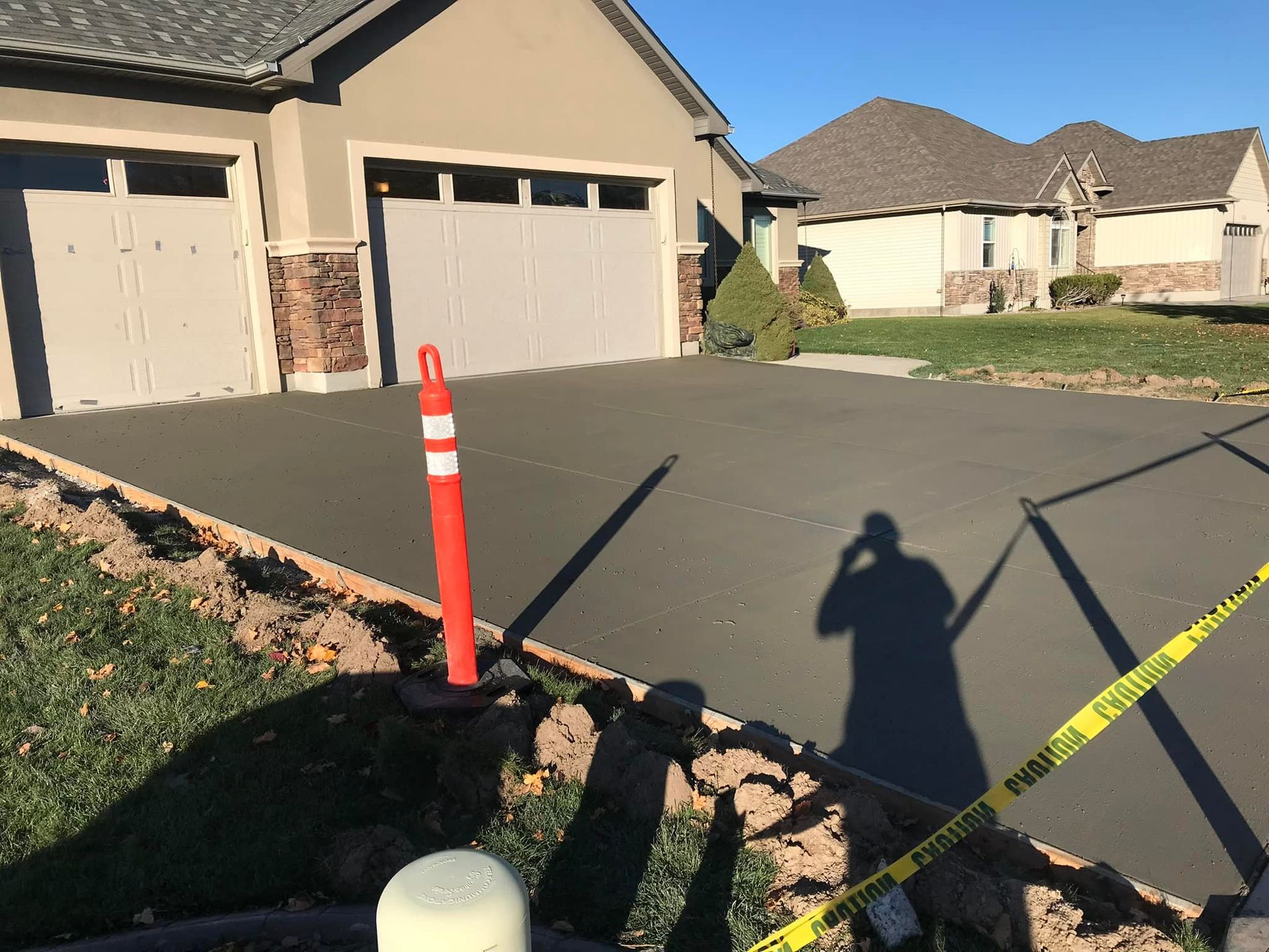 A shadow of a person is cast on a concrete driveway in front of a house