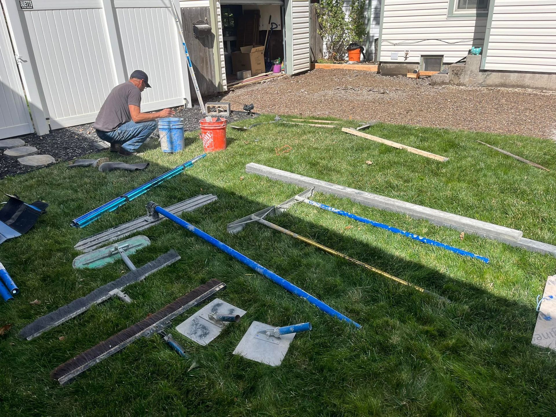 A man is kneeling down in the grass with a bunch of tools on the ground