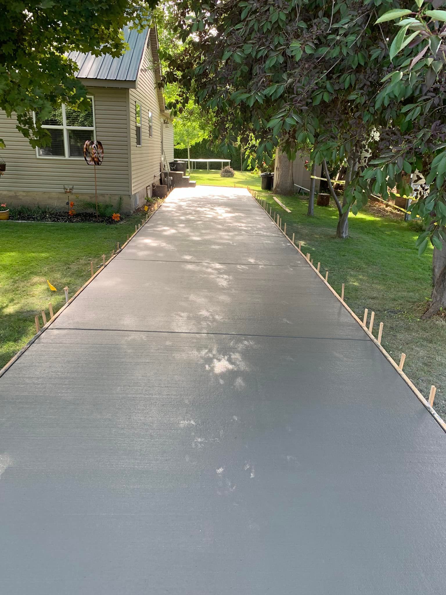 A concrete driveway leading to a house surrounded by trees and grass