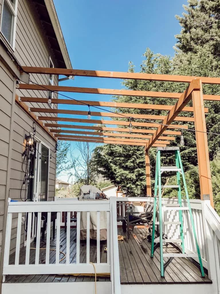 A wooden pergola is being built on the back deck of a house