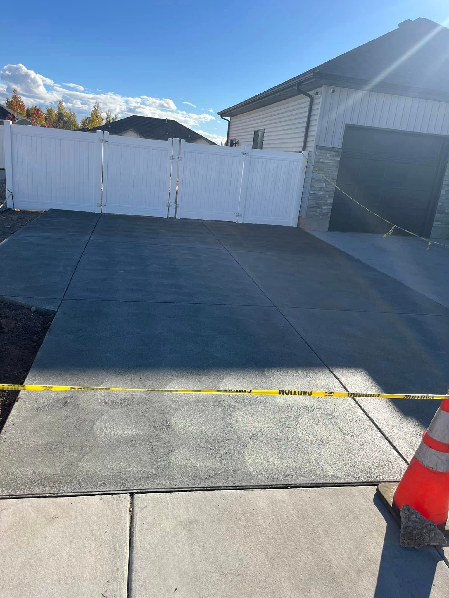 A concrete driveway with a white fence in front of a house