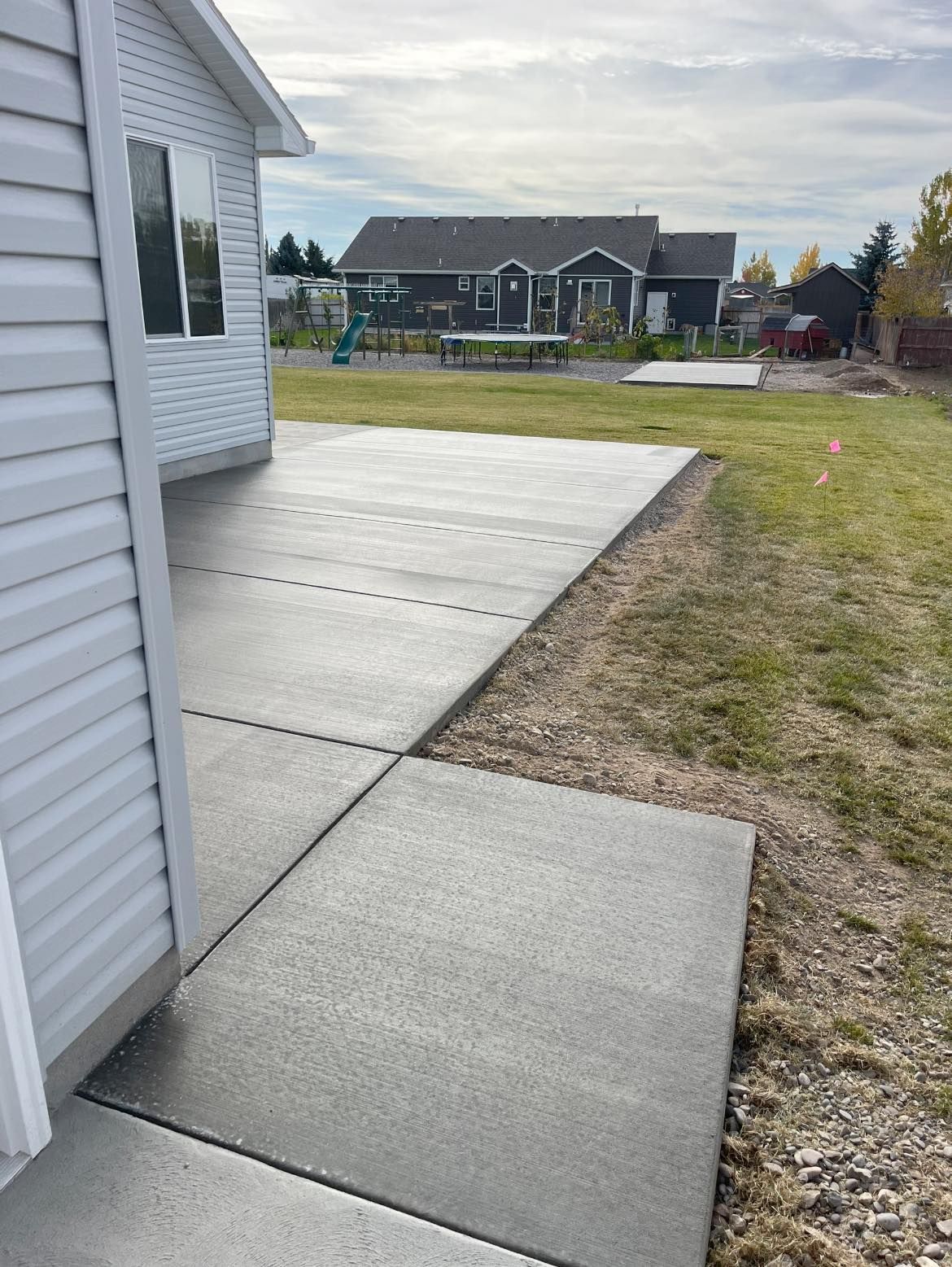 A concrete walkway leading to a house with a playground in the background