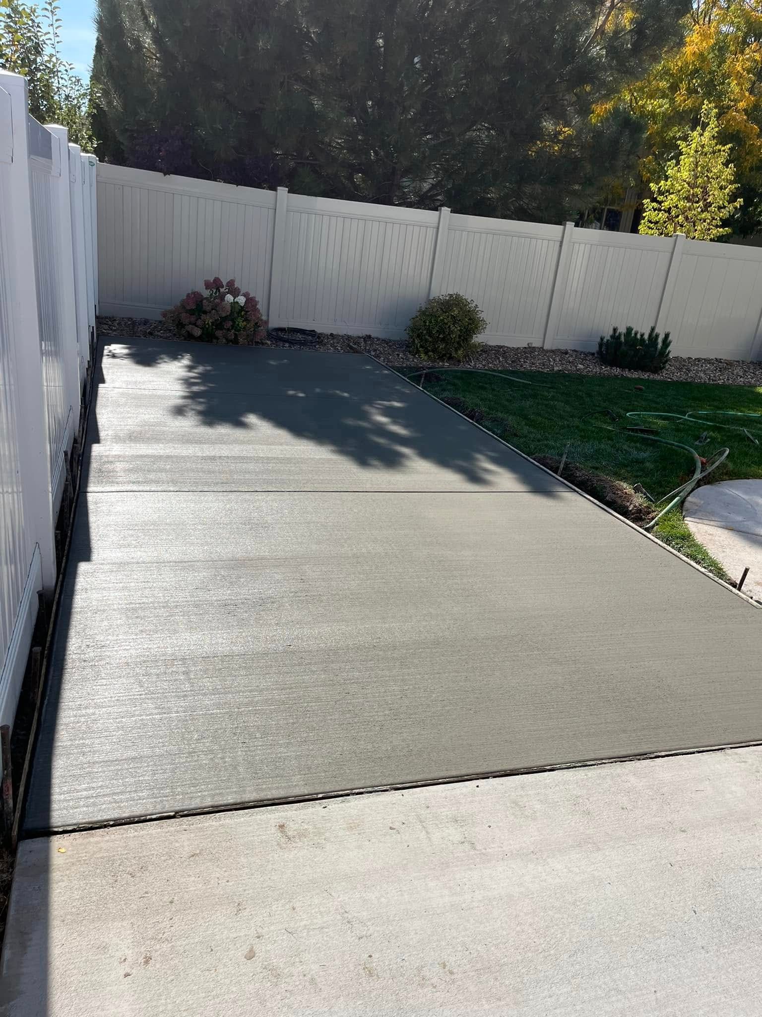 A concrete driveway with a white fence in the background