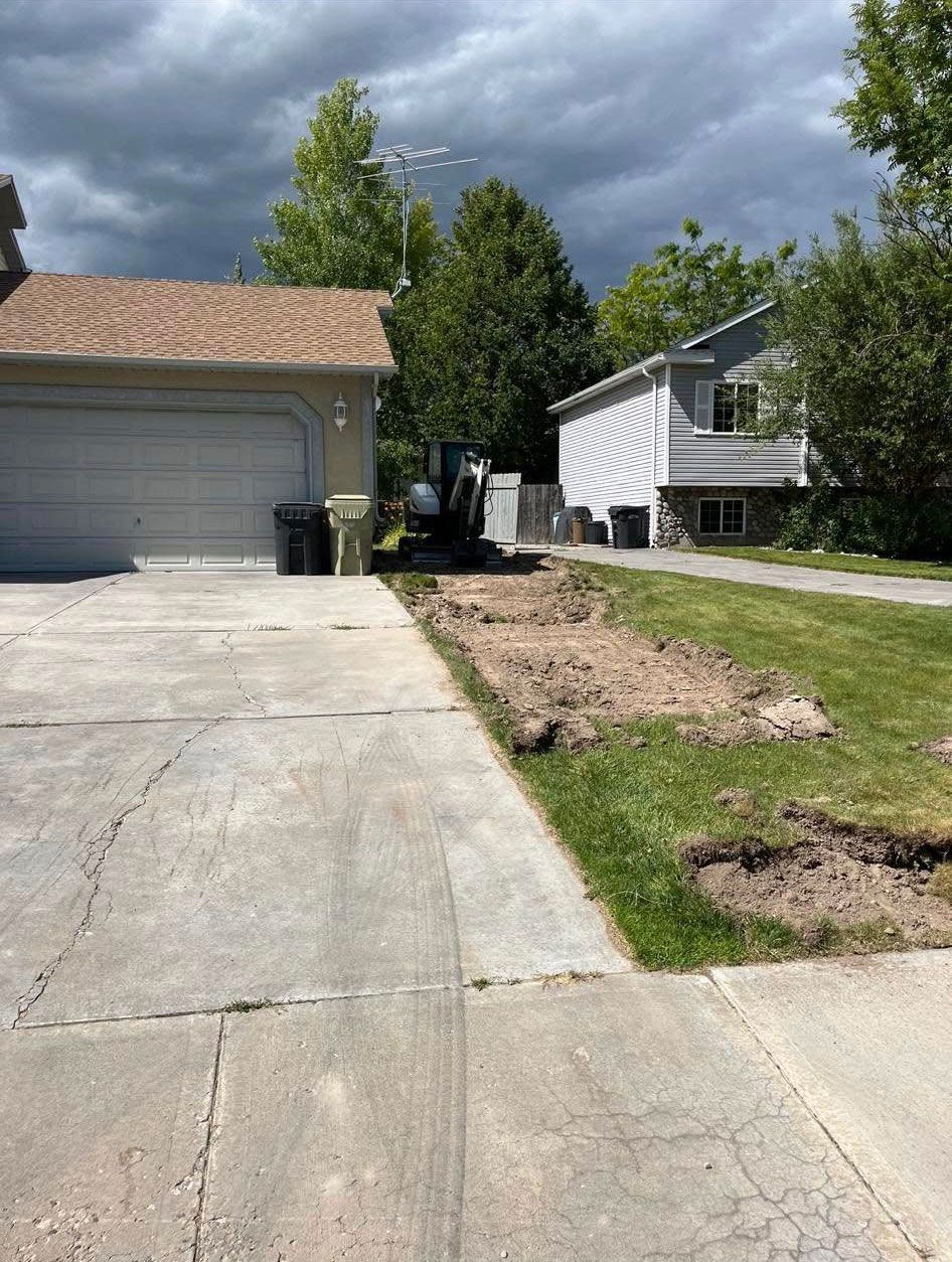 A concrete driveway leading to a house with a tractor in the background