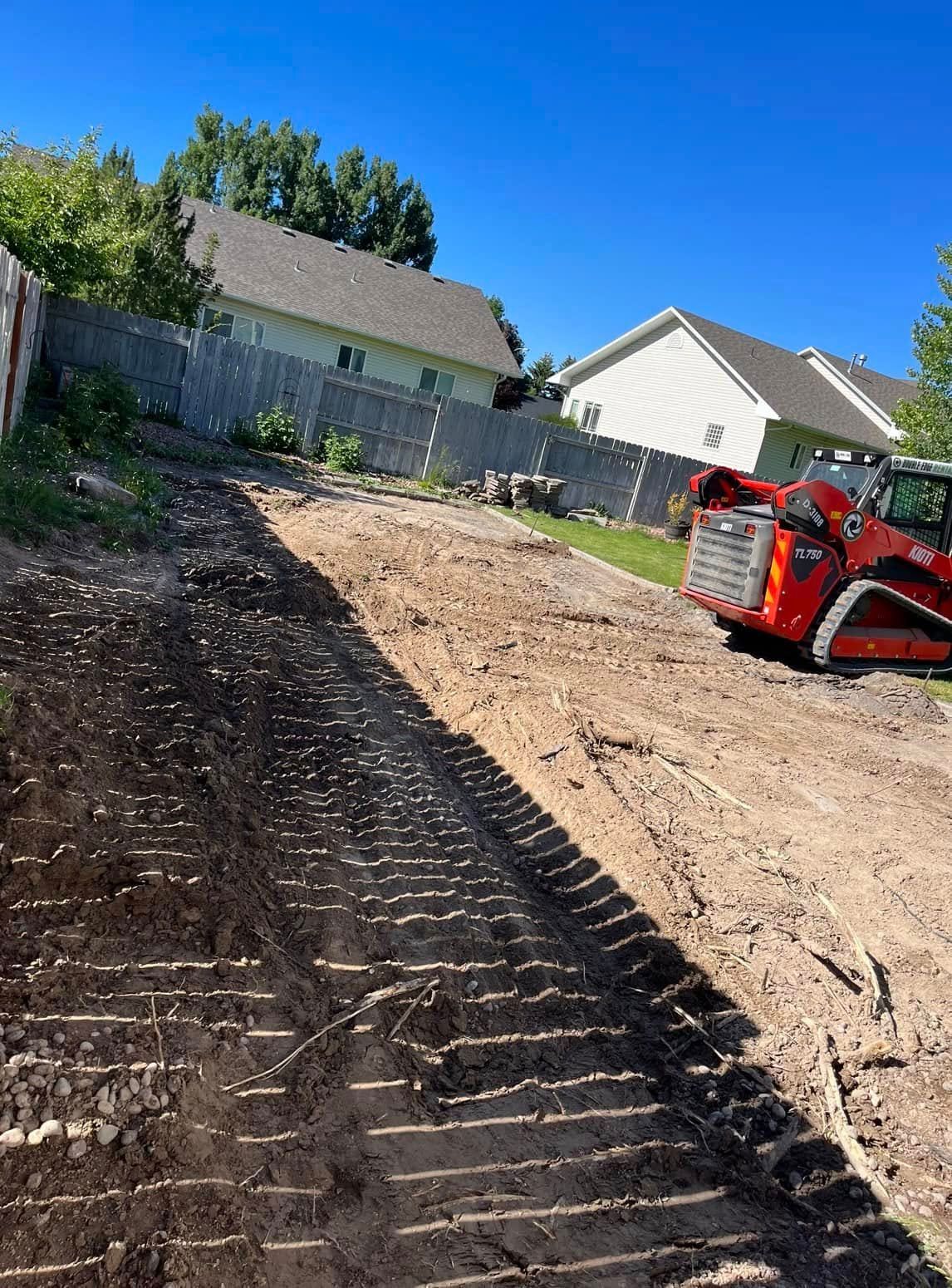 A bulldozer is driving down a dirt road next to a house