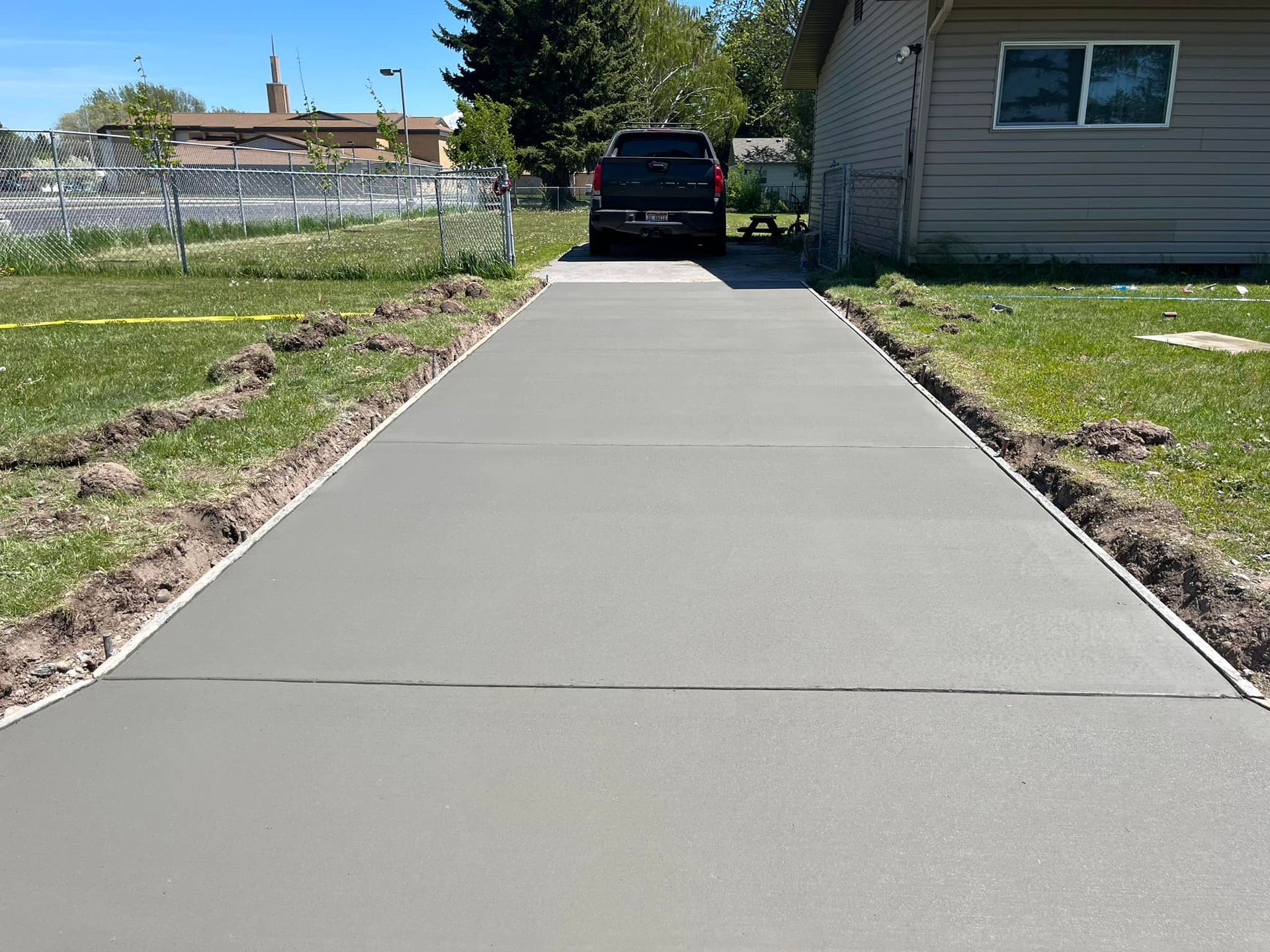 A truck is parked on the side of a concrete driveway next to a house