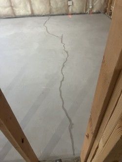 Hairline crack running across a concrete basement floor inside an unfinished room with exposed insulation and framing.