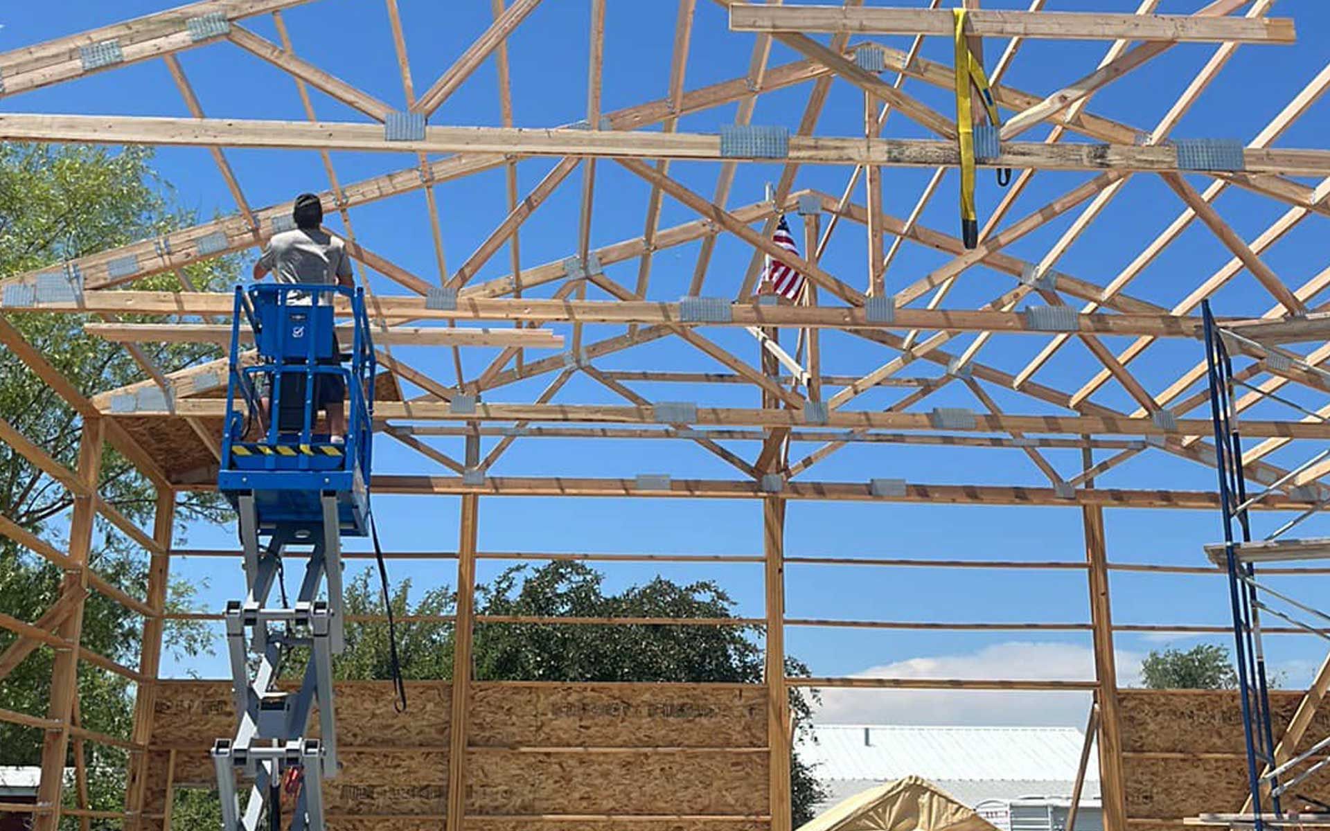 A man is standing on a lift working on the roof of a building under construction.