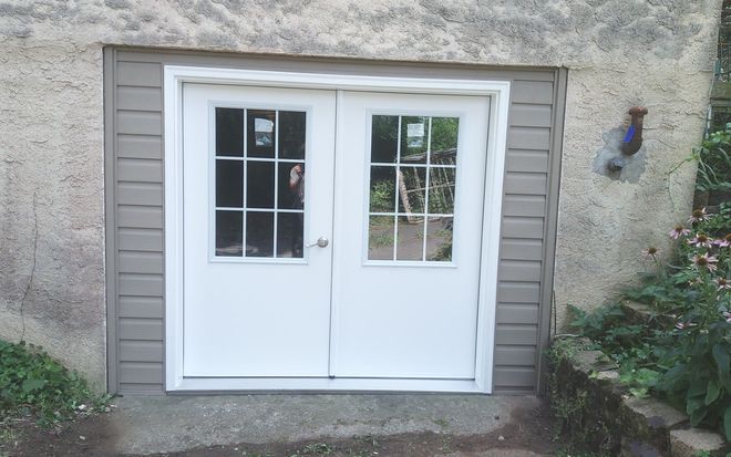 White double exterior doors with small windows set in a stone wall, framed by gray trim.