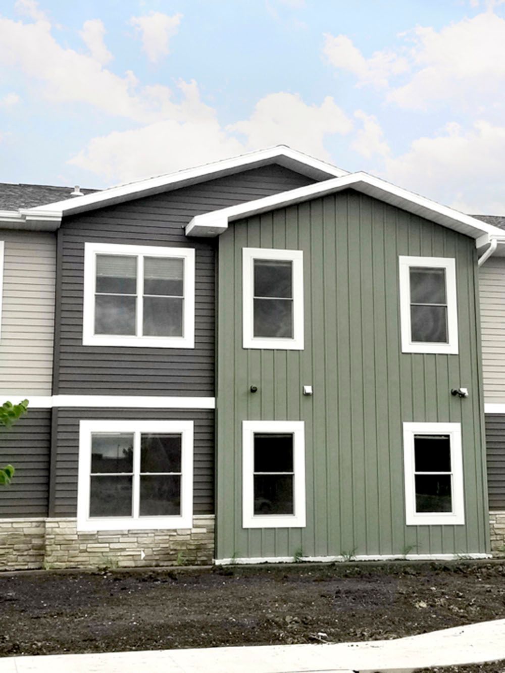 Two-story apartment building with sage green board-and-batten siding, grey horizontal siding, and stone foundation.