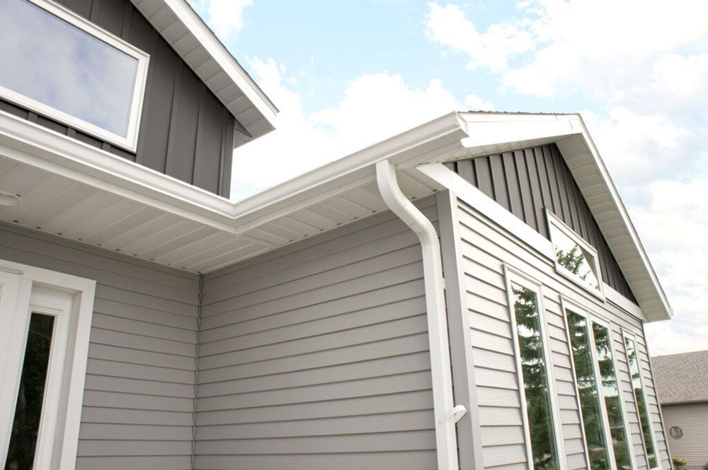 Exterior of a modern home featuring gray horizontal and vertical siding, white trim, and a white downspout.