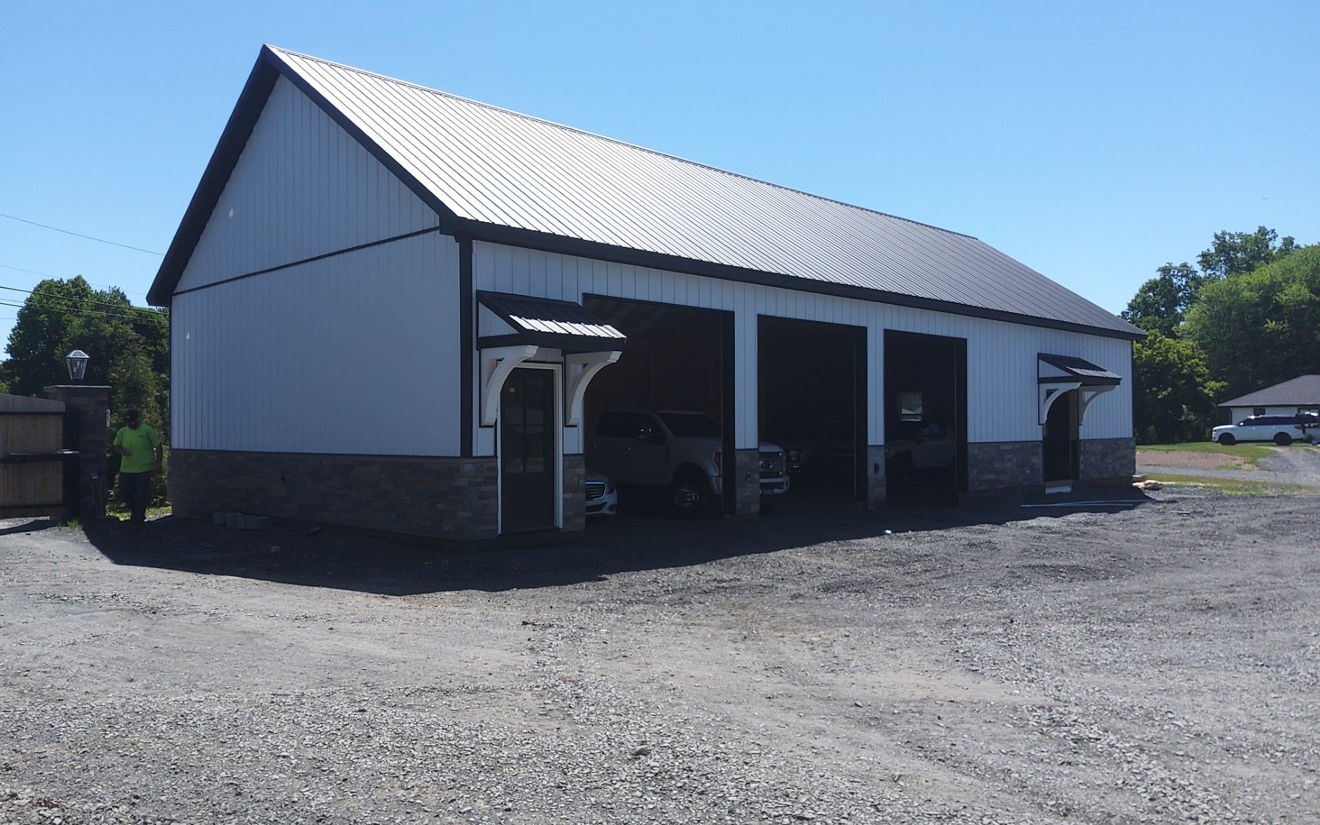 White barn-style garage with three bays on a gravel lot under a clear blue sky