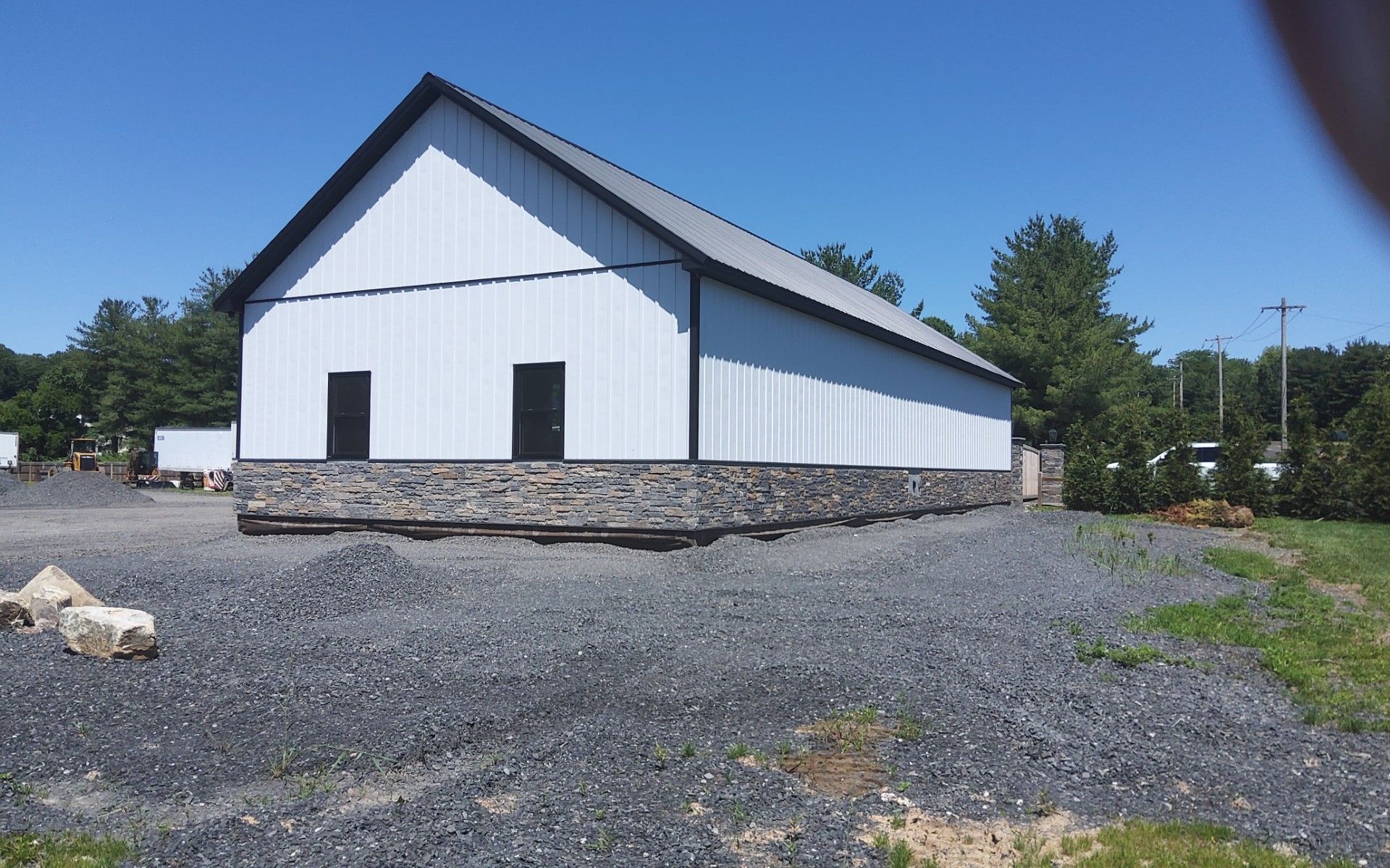 White barn-like building with blue roof trim on a gravel lot under a clear sky