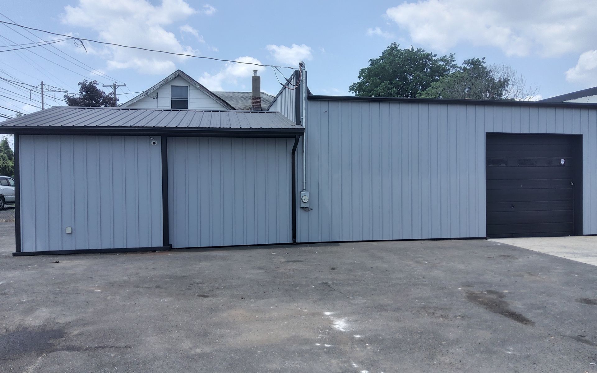 Gray metal garage building with two large doors and a dark side door beside a paved lot.