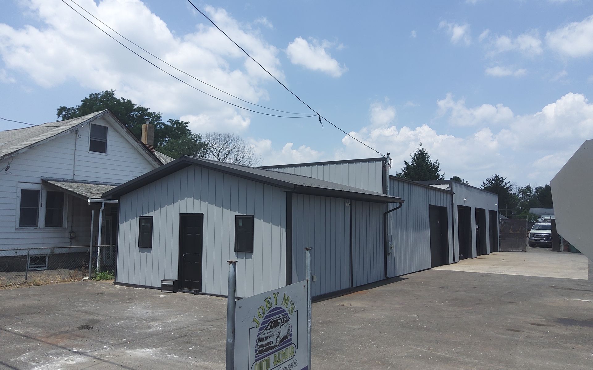 White storefront and adjacent building on a paved lot under a cloudy sky