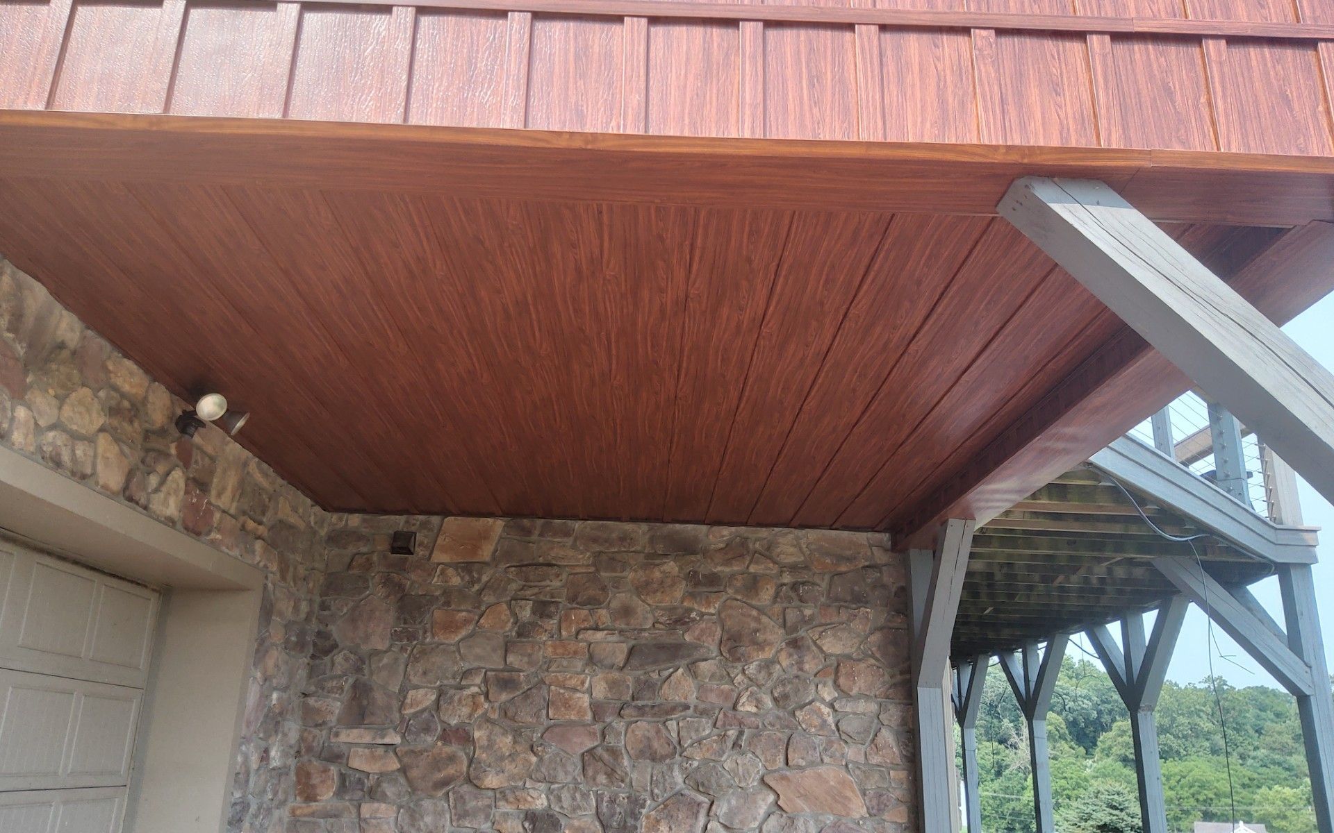 Stone house entry with wooden overhang and exposed beams, showing the roof eave and wall corner