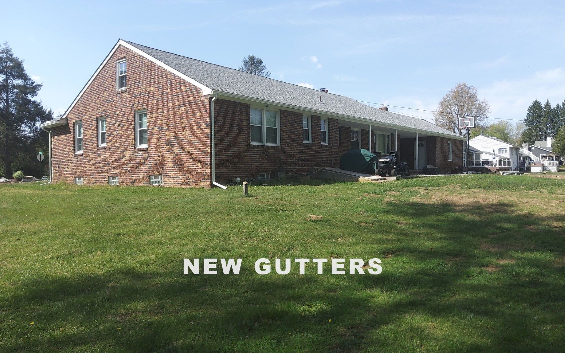 Brick house with white gutters and green lawn, labeled NEW GUTTERS