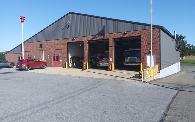 Brick auto repair garage with open bays, a red car parked outside, and a clear sky