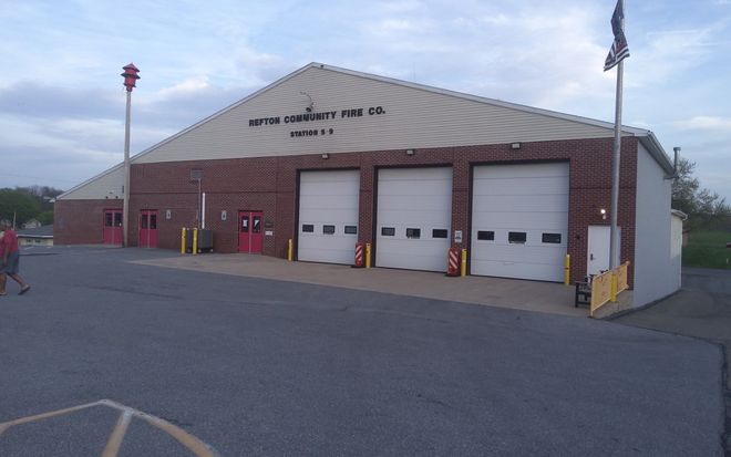 Small brick fire station with three white garage doors and a flagpole at dusk