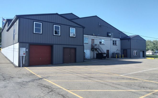Industrial building with gray siding, red garage door, and empty parking lot under a clear sky