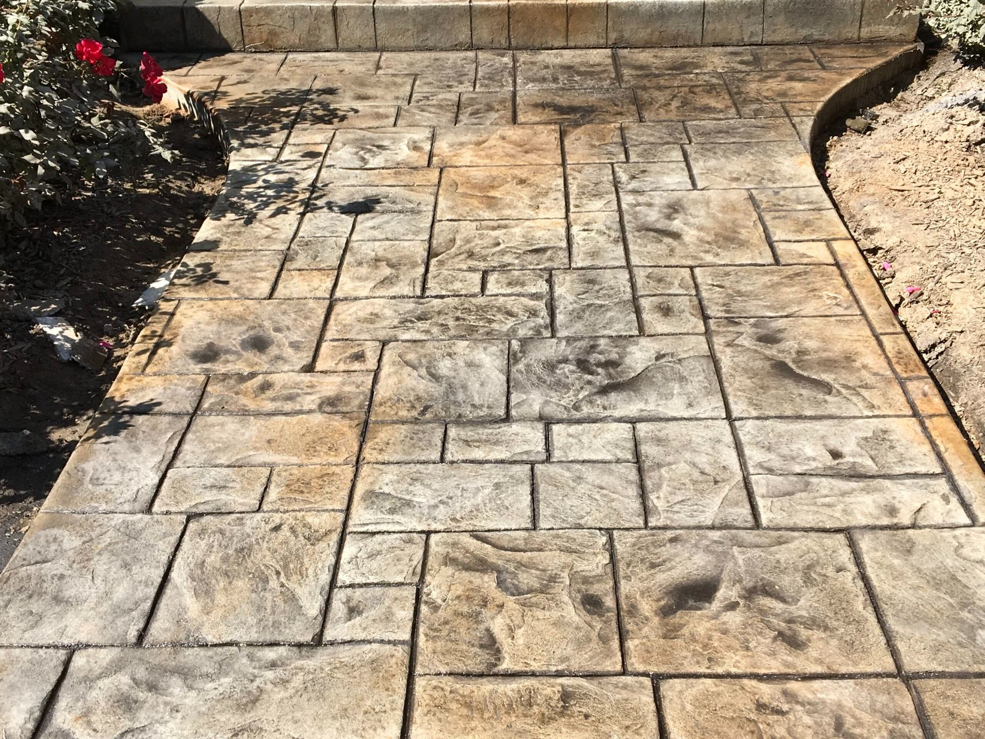 Stamped concrete walkway with rectangular and square patterns, in shades of brown and gray.
