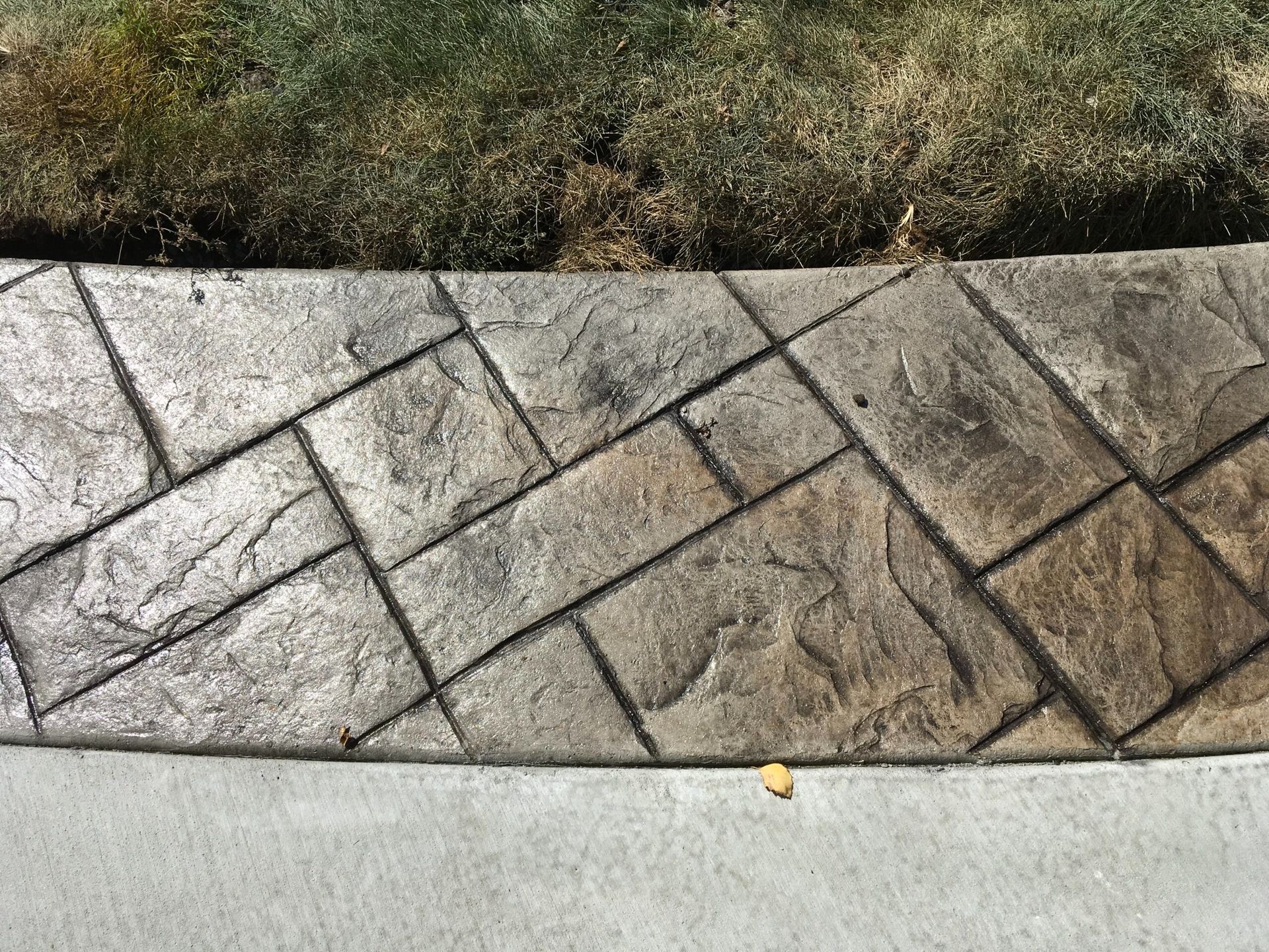 Stamped concrete border with a textured, stone-like pattern, next to lawn and sidewalk.