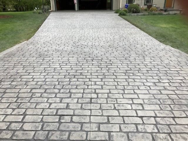 Brick-patterned concrete driveway leading to a garage, flanked by green grass.