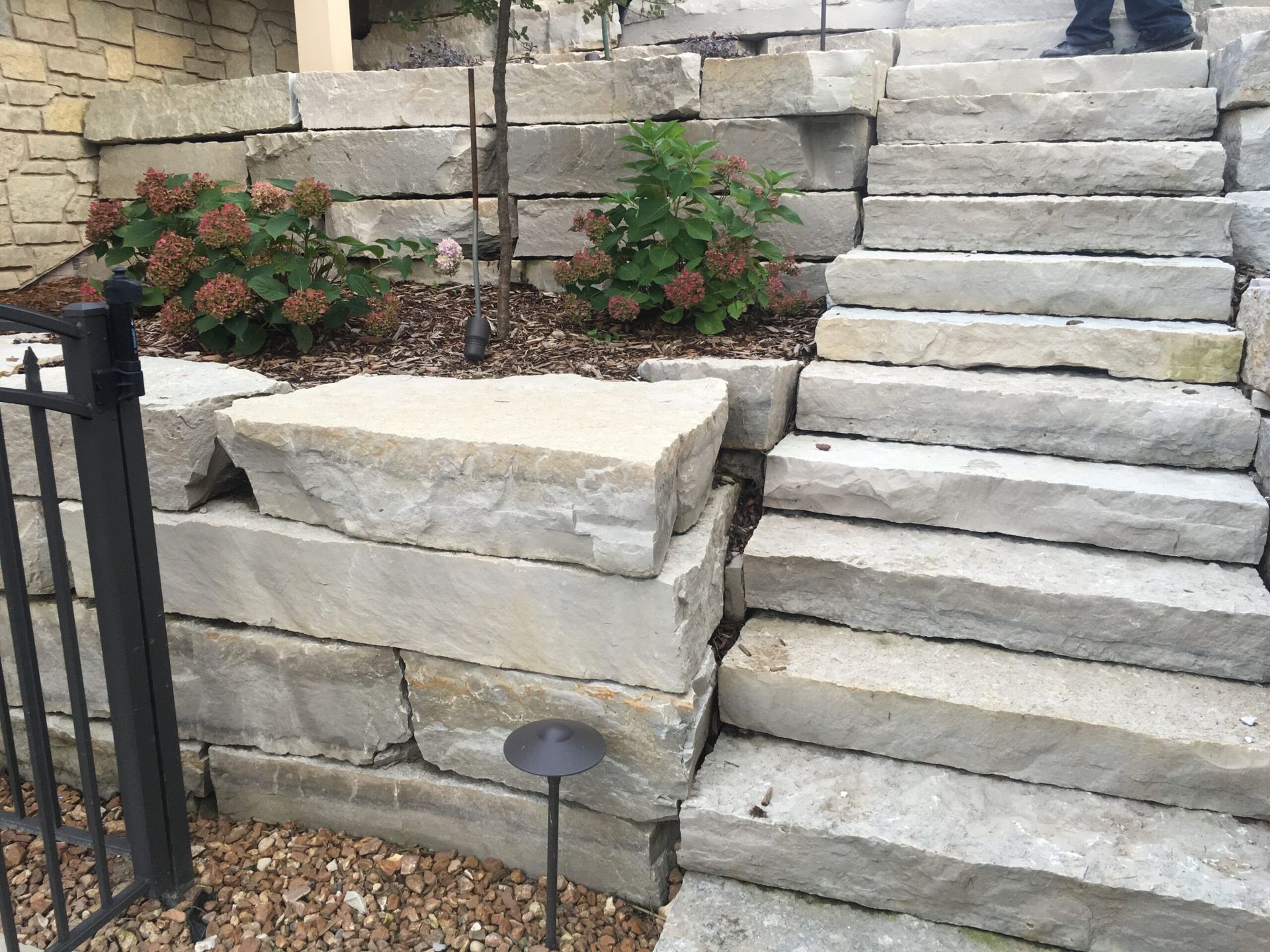 Stone steps and retaining wall with plants and a dark metal fence.